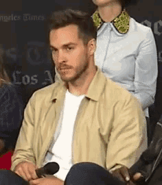 a man is sitting in a chair with a microphone in his hand and a woman is sitting behind him .
