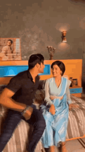 a man and a woman are sitting on a bed . the woman is wearing a blue dress .