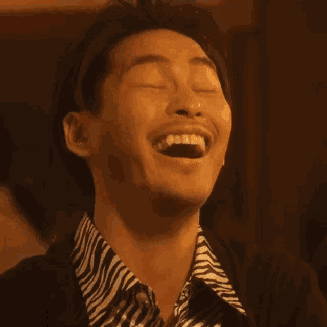 a man in a zebra print shirt is laughing with his eyes closed and his mouth open .