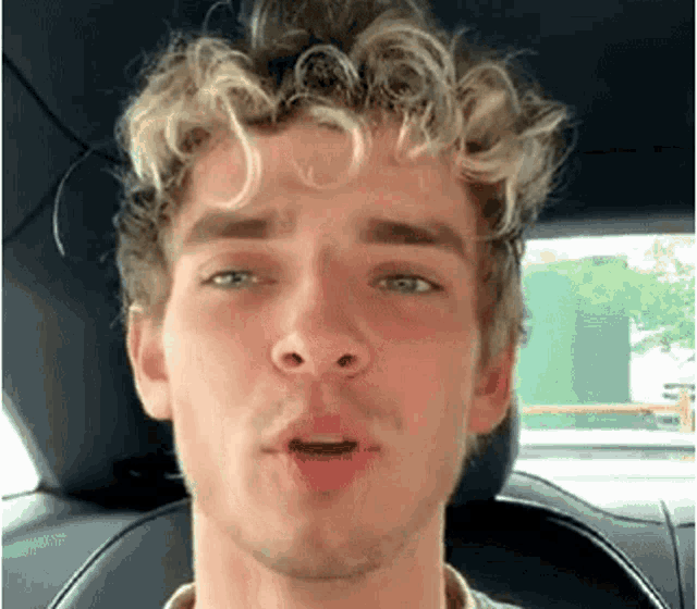 a young man with curly hair is sitting in a car with his mouth open .