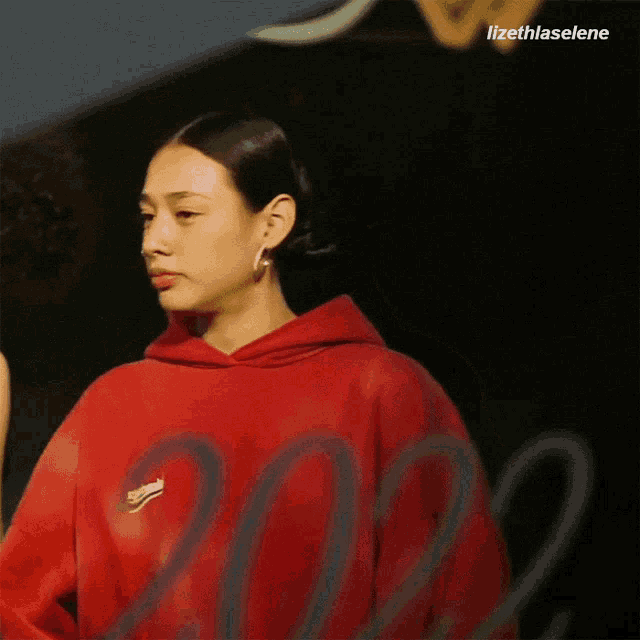 a woman wearing a red balenciaga hoodie stands in front of a sign that says 2022