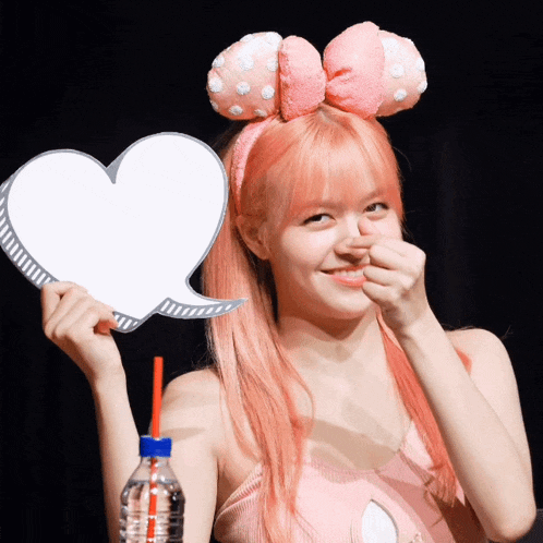 a woman with pink hair is holding a heart shaped sign