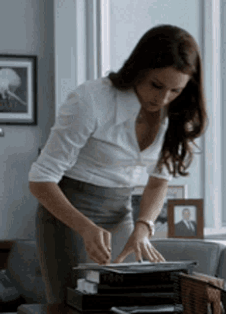 a woman in a white shirt and gray pants is standing at a desk with a stack of books on it