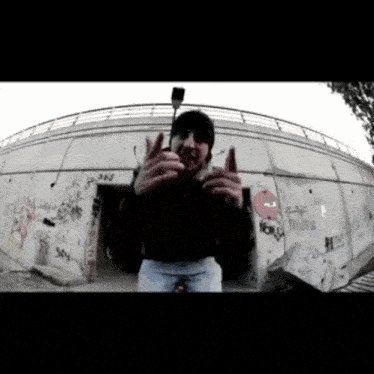 a man giving the middle finger in front of a graffiti covered wall that says ' ns ' on it