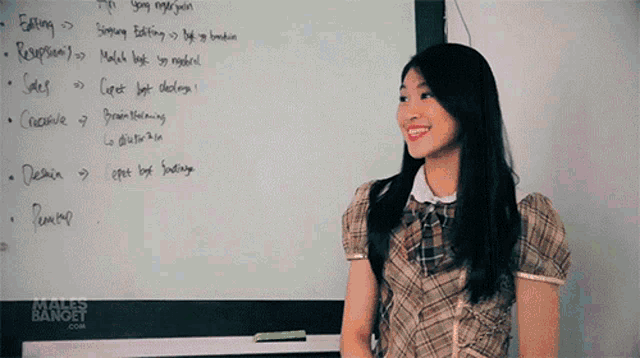 a woman stands in front of a white board with writing on it including editing
