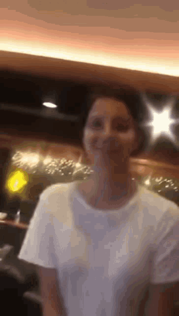 a woman wearing a white t-shirt is smiling in a blurry photo .