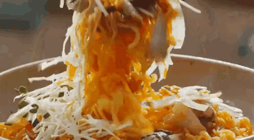 a close up of a bowl of food with noodles and cheese being poured into it