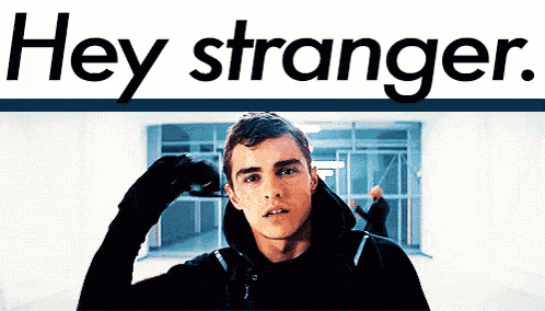 a young man in a black hoodie is standing in front of a sign that says hey stranger