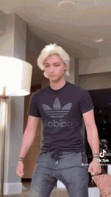 a young man with blonde hair is wearing a black adidas t-shirt and gray pants .