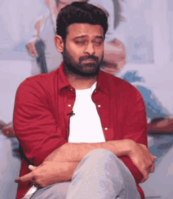 a man wearing a red shirt and a white shirt is sitting with his arms crossed