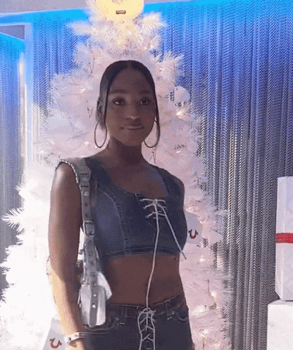 a woman in a crop top is standing in front of a white christmas tree .