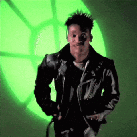 a man in a black leather jacket is standing in front of a green light .