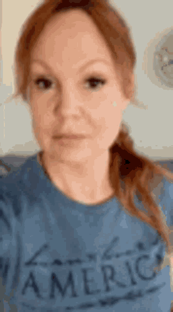 a woman with red hair is wearing a blue t-shirt that says `` liberty america '' .