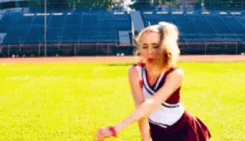 a cheerleader in a maroon and white uniform is standing in the grass