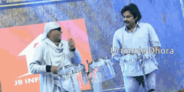 two men playing drums in front of a jb info sign
