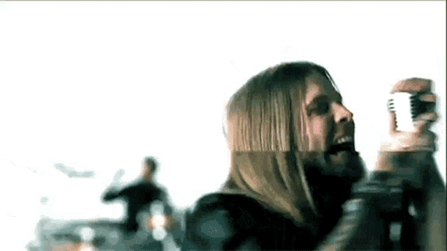 a man with long hair and a beard is singing into a microphone in front of a crowd .