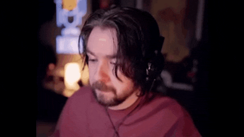 a man with a beard wearing headphones and a red shirt is sitting in front of a computer screen .