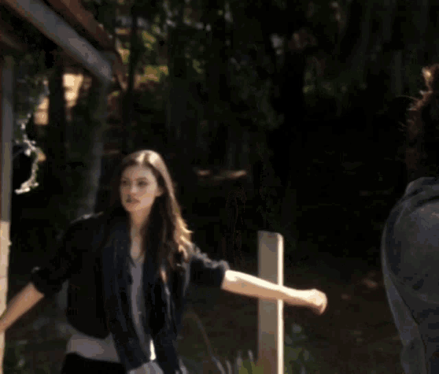 a woman in a black jacket stands in front of a wooden post