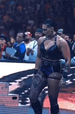 a woman is standing on a stage in front of a crowd in a wrestling ring .