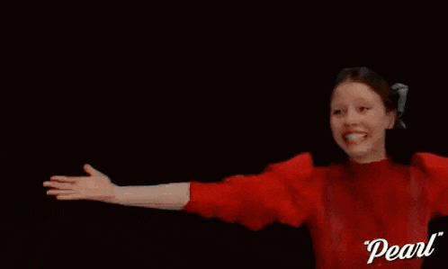 a woman in a red sweater is laughing with her arms outstretched in the air .