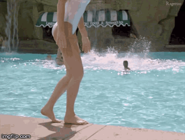 a woman in a bathing suit walks by a pool with a waterfall in the background and a sign that says food & smoothies