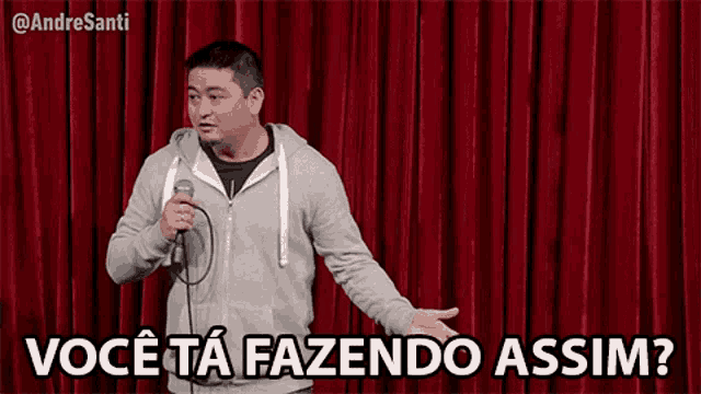 a man is holding a microphone in front of a red curtain and says você ta fazendo assim