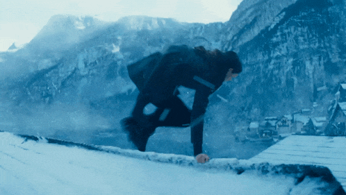 a man in a black jacket is jumping over a snowy railing