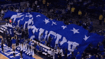 a large blue and white kentucky flag is being displayed on a basketball court
