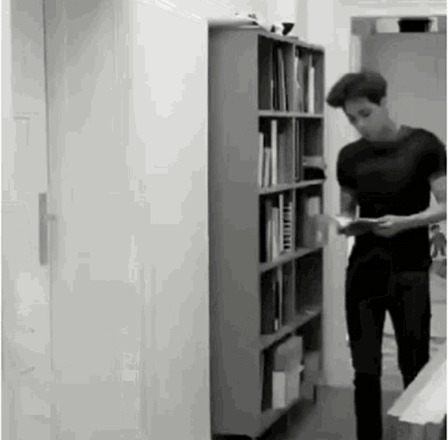 a man is standing in front of a bookshelf holding a book .