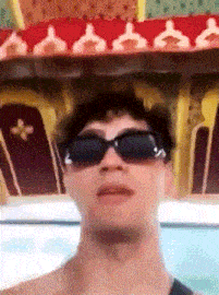 a man wearing sunglasses is making a funny face while standing in front of a coffin .