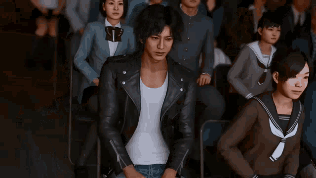 a man wearing a leather jacket is standing in front of a crowd of people .