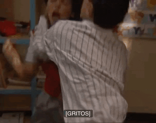 a man in a striped shirt is holding another man in his arms while another man says gritos .