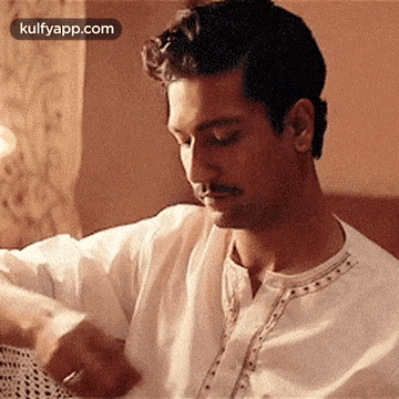 a man in a white shirt is sitting on a couch looking down at something .