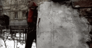 a man in a red scarf is standing next to a brick wall smoking a cigarette
