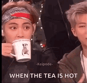 a man is drinking a cup of tea while another man watches .