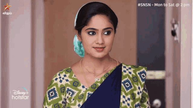 a woman in a blue and green saree is standing in front of a door and smiling .