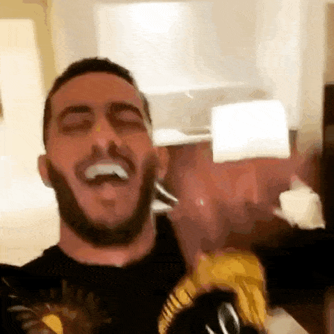 a man with a beard is laughing and holding a bottle of beer in his hand .