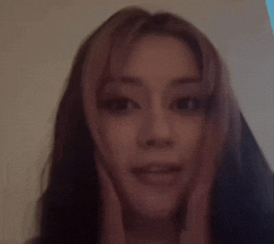 a close up of a woman 's face with pink hair and a blurry background .