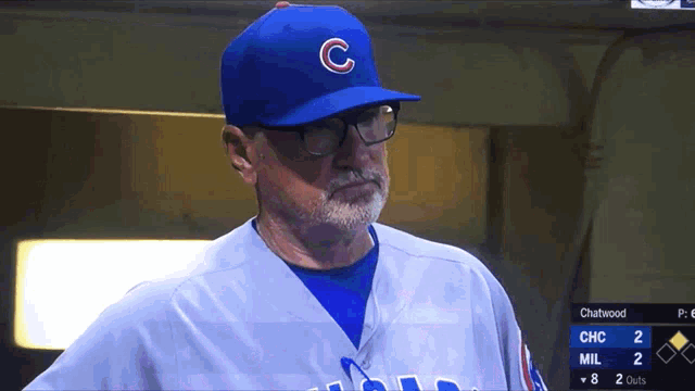 a man wearing a blue cubs hat and glasses stands in the dugout