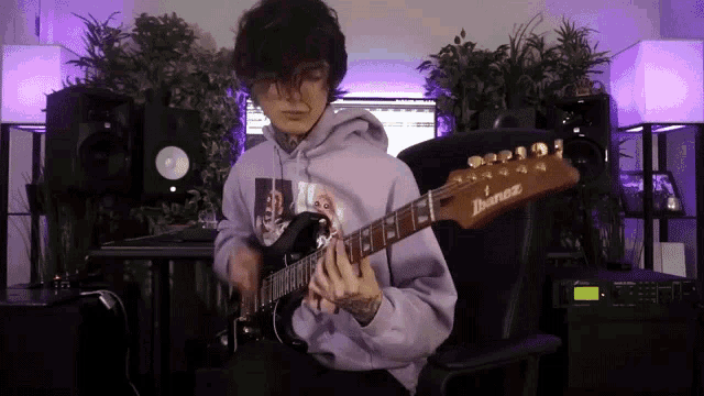 a man in a purple hoodie is playing an ibanez electric guitar