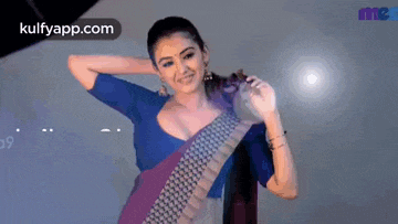 a woman in a saree is smiling and dancing in front of a light .