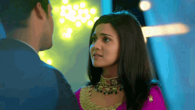 a man and woman are looking at each other and the woman is wearing a necklace
