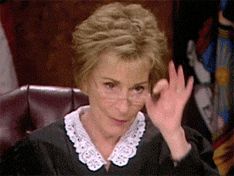 a female judge wearing glasses and a lace collar is giving a thumbs up