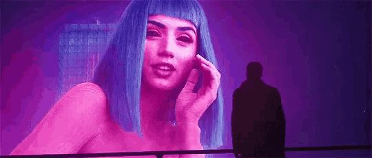 a man is standing in front of a screen with a woman in blue wig on it .
