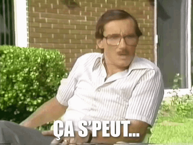 a man with glasses and a mustache is sitting in front of a brick building and says ca s ' peut .