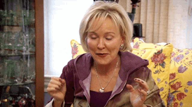 a woman is sitting on a couch in a living room with a yellow pillow and a purple jacket .