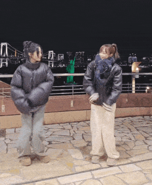 two women are dancing in front of the statue of liberty at night