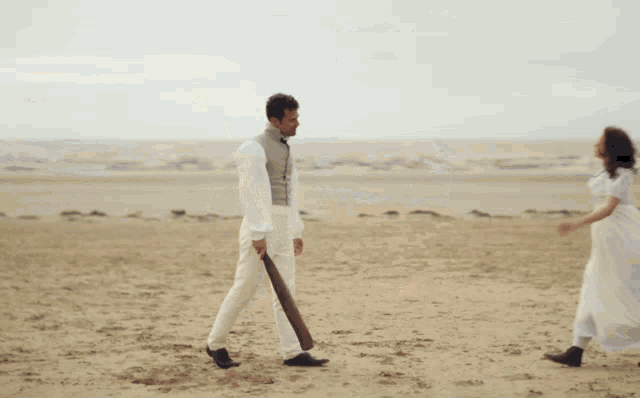 three men are standing on a sandy beach and one is wearing a vest