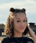 a young woman with curly hair is wearing a black shirt and a necklace and smiling .