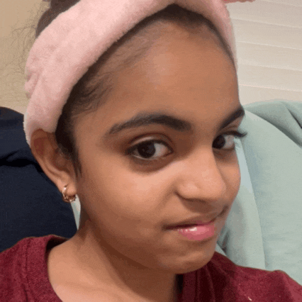 a young girl wearing a pink headband and earrings looks at the camera